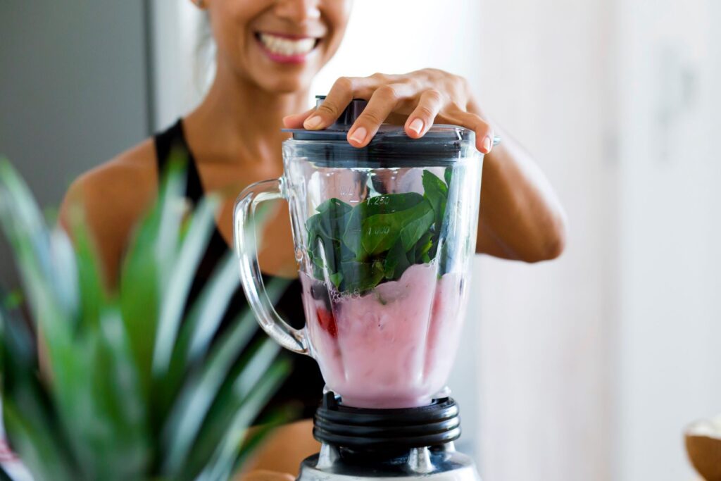 Woman blending spinach, fruit, and yogurt with blender